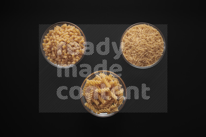 Different pasta types in glass bowls on black background