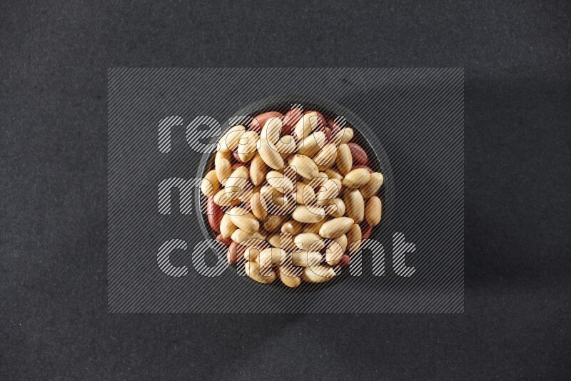 A black pottery bowl full of peeled peanuts on a black background in different angles