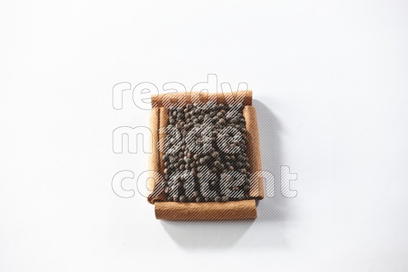 A single square of cinnamon sticks full of black pepper on white flooring
