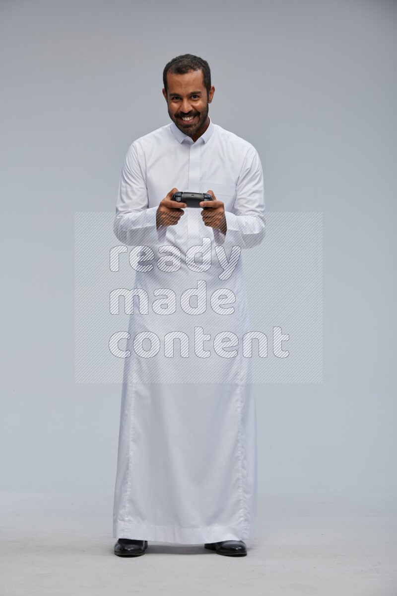 Saudi man Wearing thob standing holding joystick on Gray background