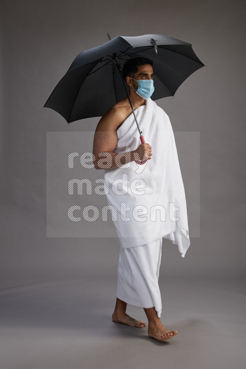 A man wearing Ehram and mask Standing holding umbrella on gray background on gray background