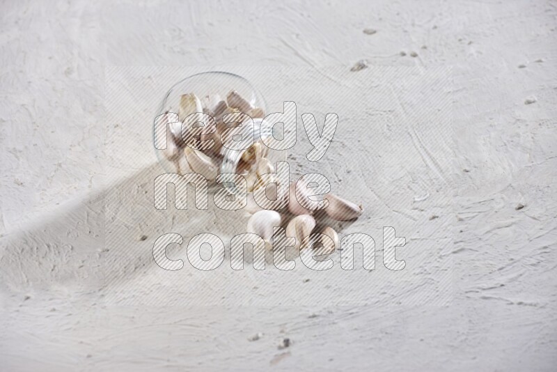 A glass spice jar full of garlic cloves flipped over with the cloves spilling out on a textured white flooring