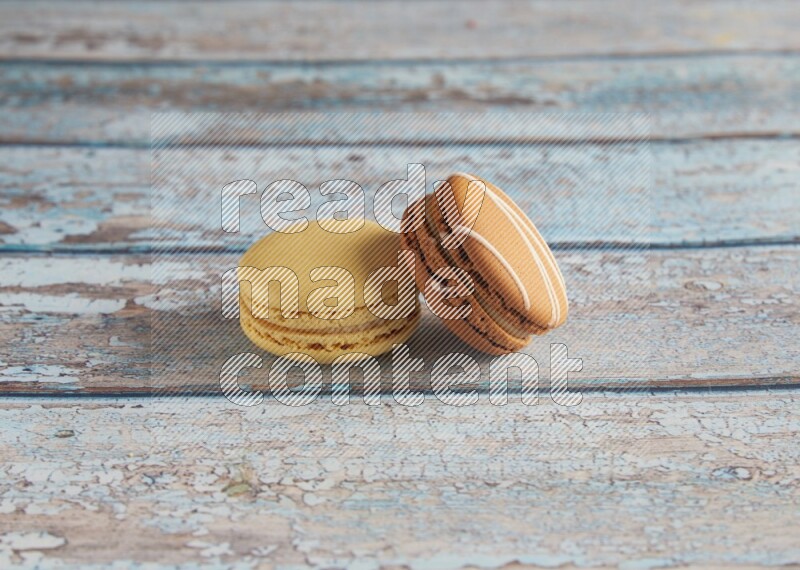 45º Shot of of two assorted Brown Irish Cream, and Yellow Vanilla macarons on light blue background