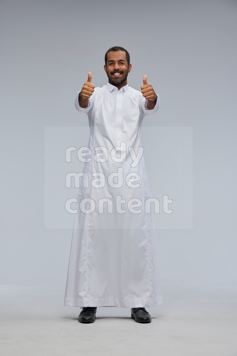 Saudi man Wearing Thob standing interacting with the camera on Gray background