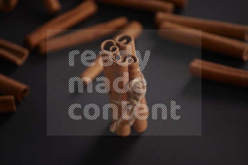 4 Cinnamon sticks stacked and bounded with more sticks in the background on black flooring