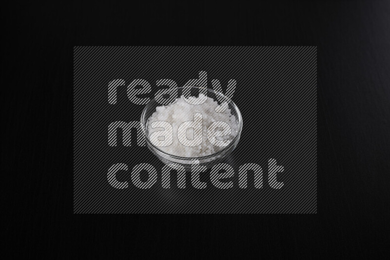 وعاء زجاجي ممتلئ بملح البحر الخشن على خلفية سوداء