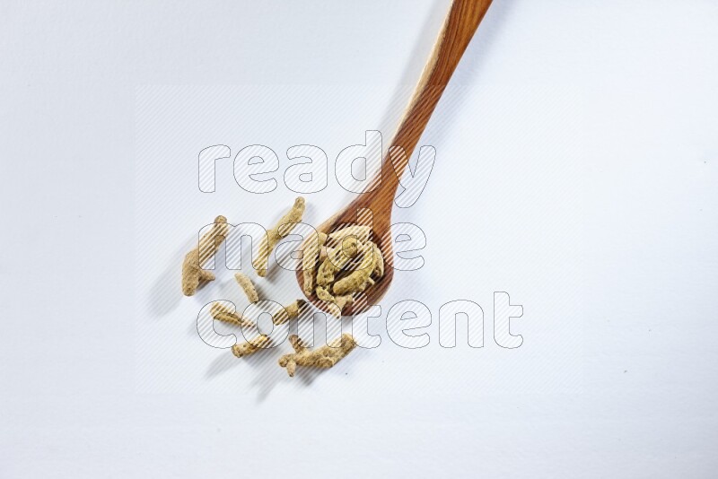 A wooden ladle full of dried turmeric fingers on white flooring