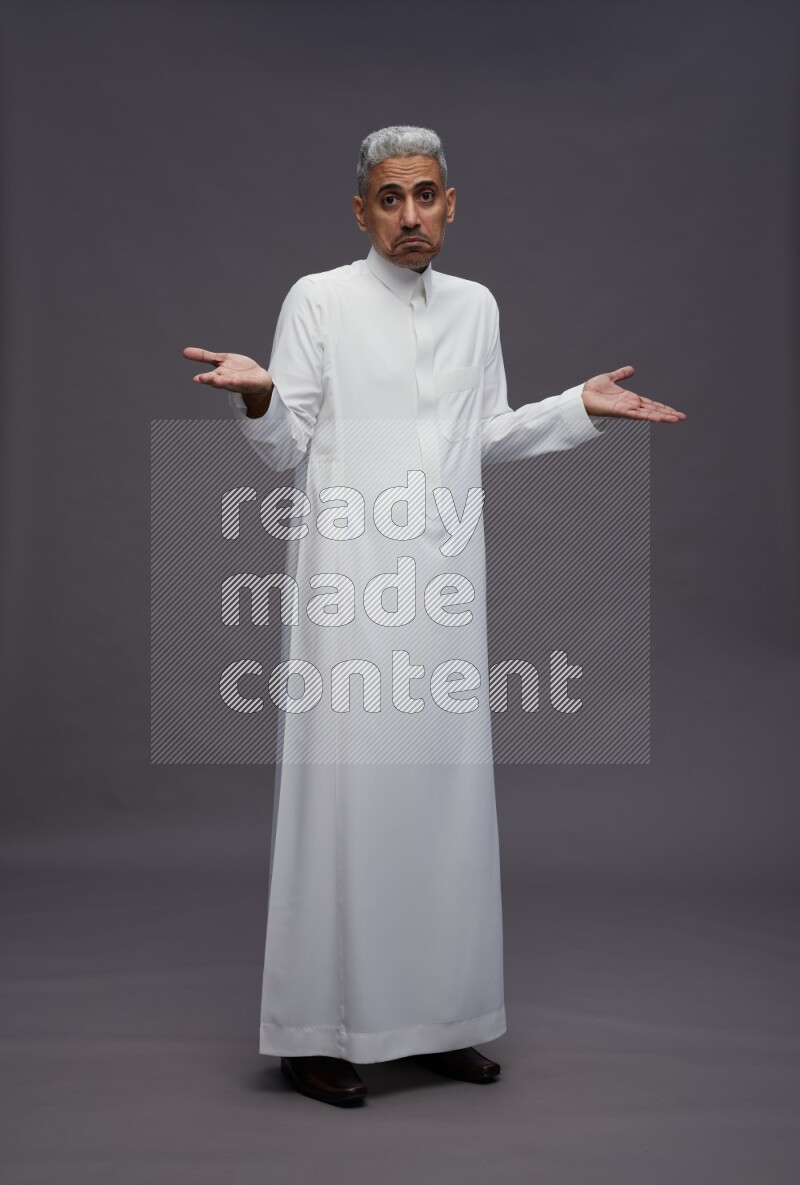 Saudi man wearing thob standing interacting with the camera on gray background
