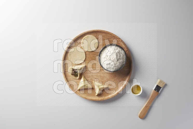 two closed sambosas and one open sambosa filled with meat while flour, and oil with oil brush aside in a wooden dish on a white background