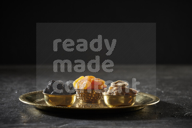 Dried fruits in metal bowls on a tray in a dark setup