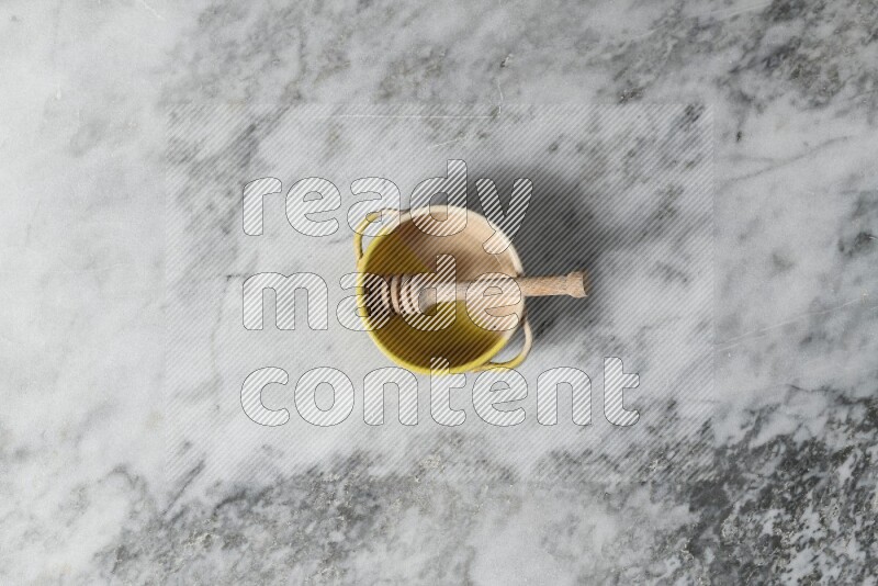 Multicolored pottery bowl with wooden honey dipper in it on grey marble background