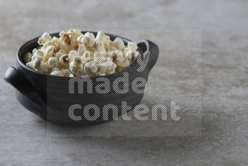 popcorn in a black handheld ceramic bowl on a grey textured countertop