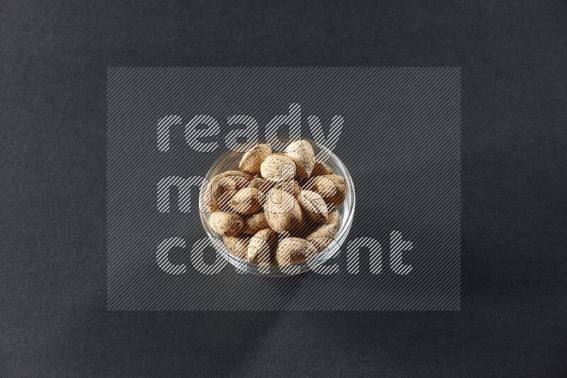 A glass bowl full of almonds on a black background in different angles