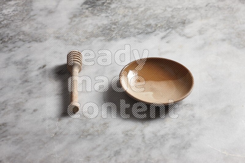 Multicolored pottery plate with wooden honey dipper on the side on grey marble background