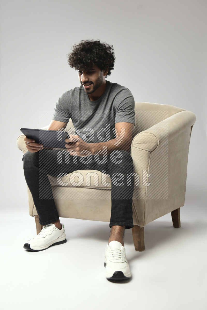 A man wearing casual sitting on a chair gaming on a tablet on white background