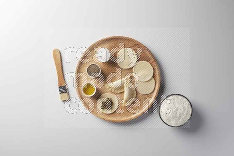 two closed sambosas and one open sambosa filled with meat while flour, salt, black pepper and oil with oil brush aside in a wooden dish on a white background