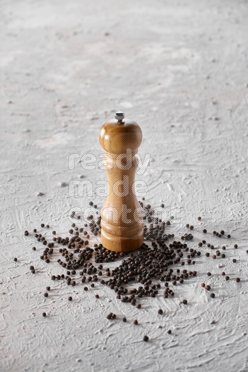 A wooden grinder with black pepper beads on a textured white flooring