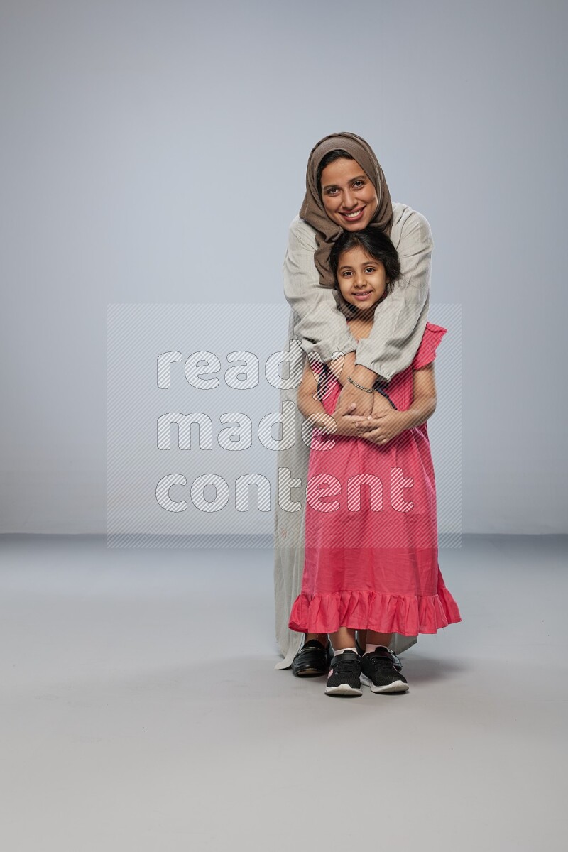 A girl and her mother interacting with the camera on gray background