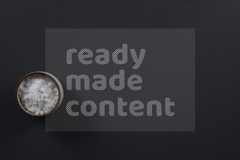 Pottery bowl full of fine table salt and coarse sea salt on black background