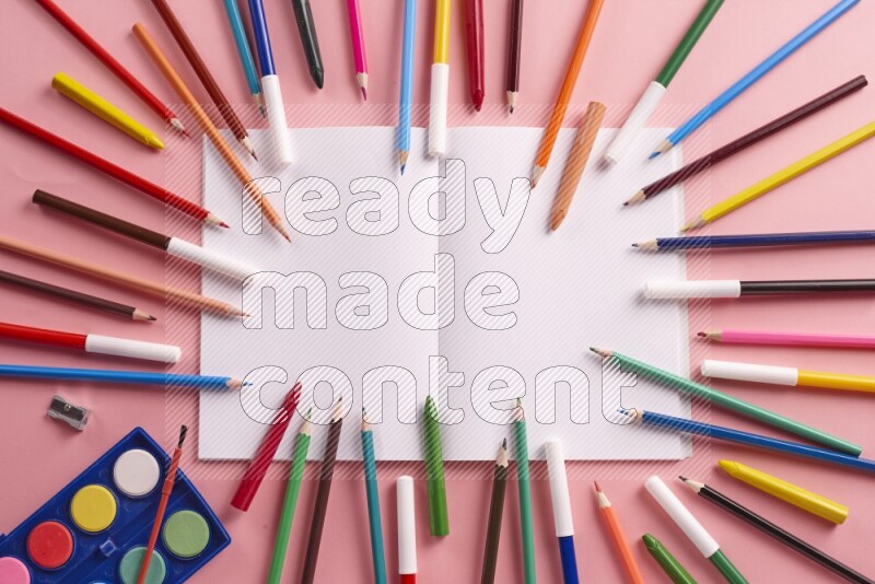 دفتر فارغ مفتوح مع أقلام تلوين على خلفية وردية