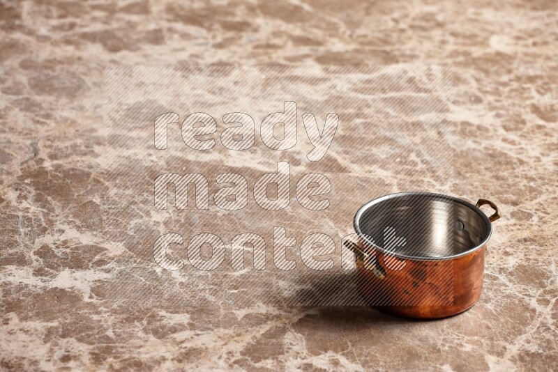 A small copper pot on beige marble background