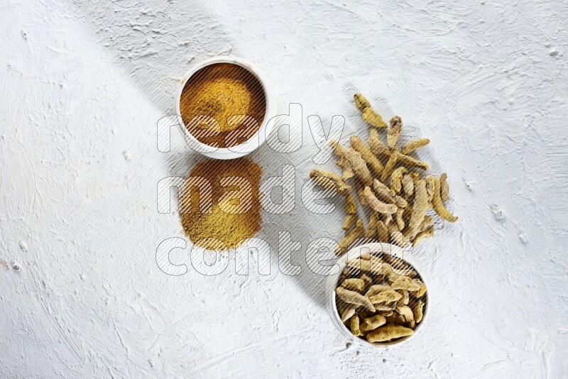 2 beige pottery bowls full of turmeric powder and dried turmeric whole fingers with powder and fingers next of it textured white flooring