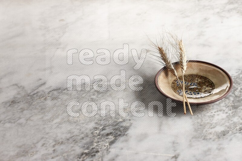 Wheat stalks on decorative pottery plate on grey marble background