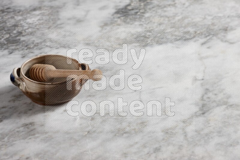 Multicolored pottery bowl with wooden honey dipper in it on grey marble background