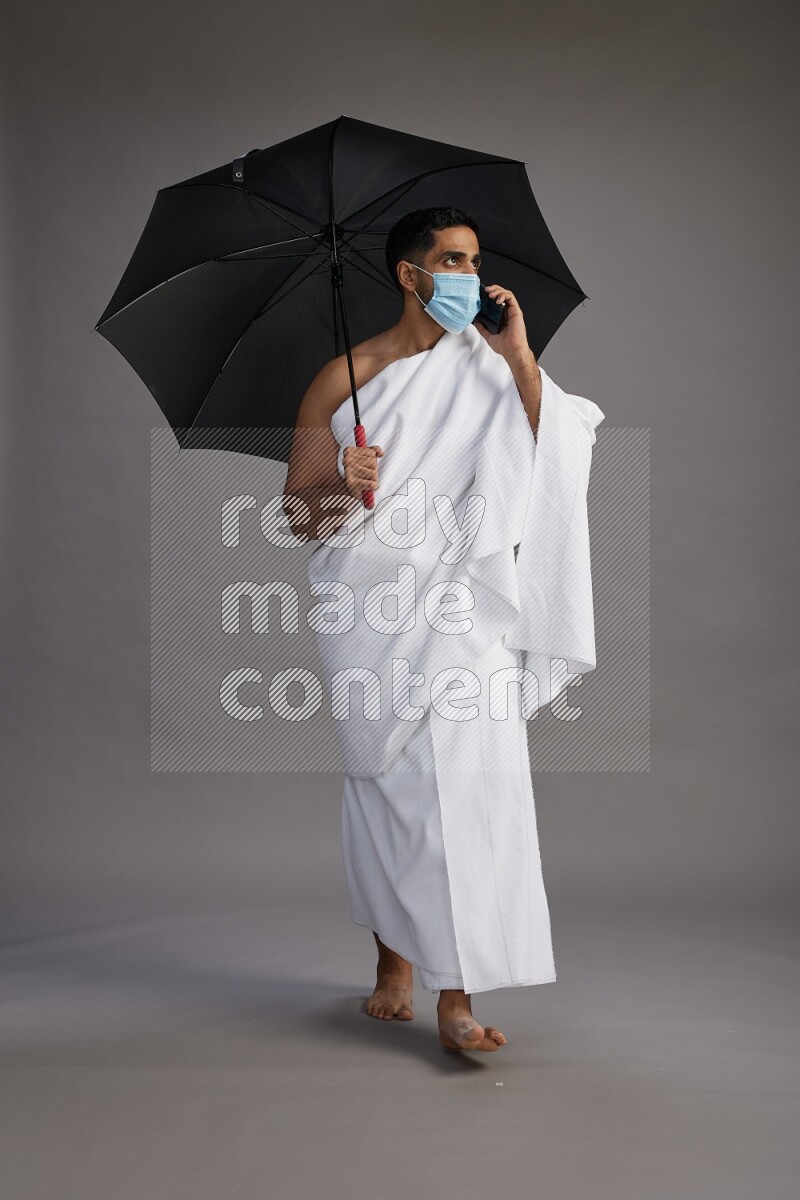 A man wearing Ehram and mask Standing holding umbrella on gray background on gray background