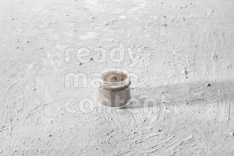 A glass jar full of black pepper powder on a textured white flooring