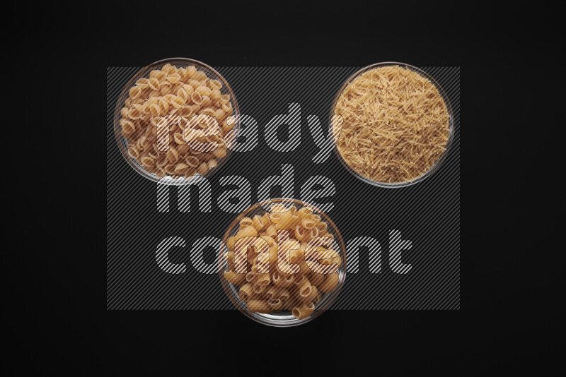 Different pasta types in glass bowls on black background