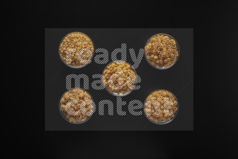Different pasta types in 5 glass bowls on black background