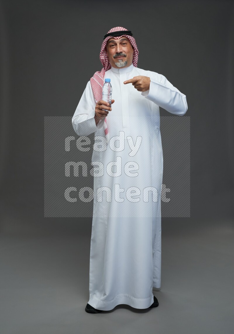 Saudi man with shomag Standing drinking water on gray background