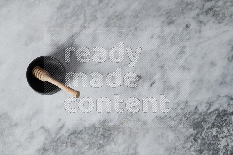 وعاء فخاري أسود مع ملعقة عسل خشبية بداخله على خلفية من الرخام الرمادي