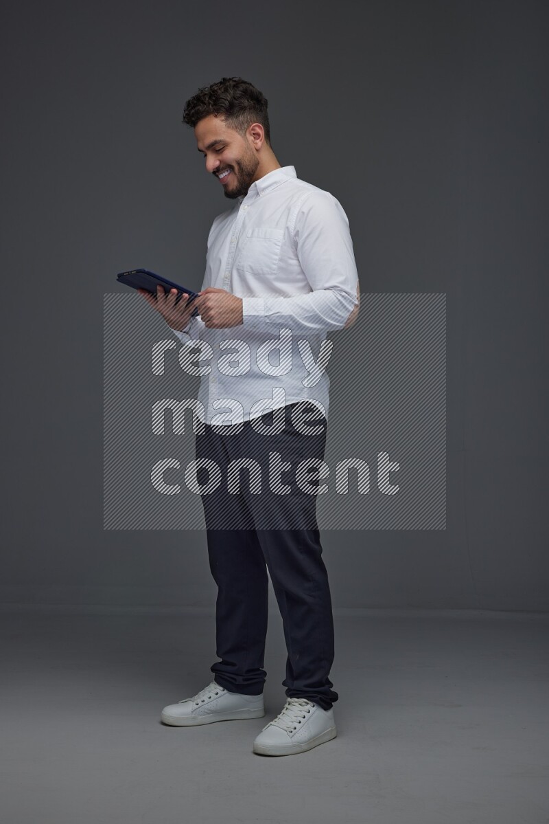 A man wearing smart casual standing and using his tablet eye level on a gray background
