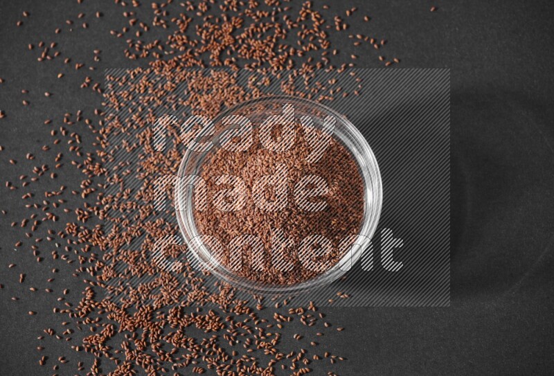 وعاء زجاجي ممتلئ ببذور حب الرشاد محاط بالبذور على أرضية سوداء