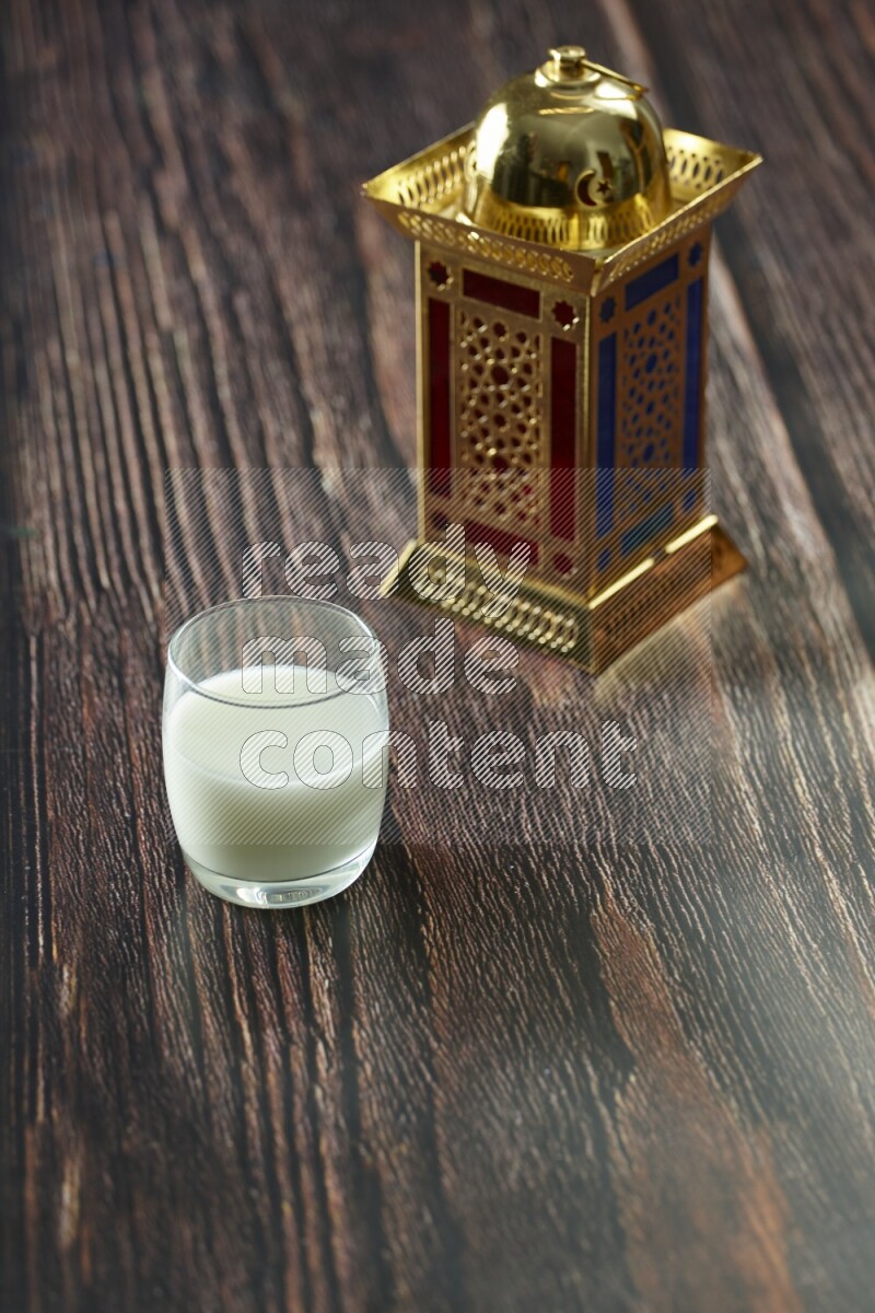 A golden lantern with different drinks, dates, nuts, prayer beads and quran on brown wooden background