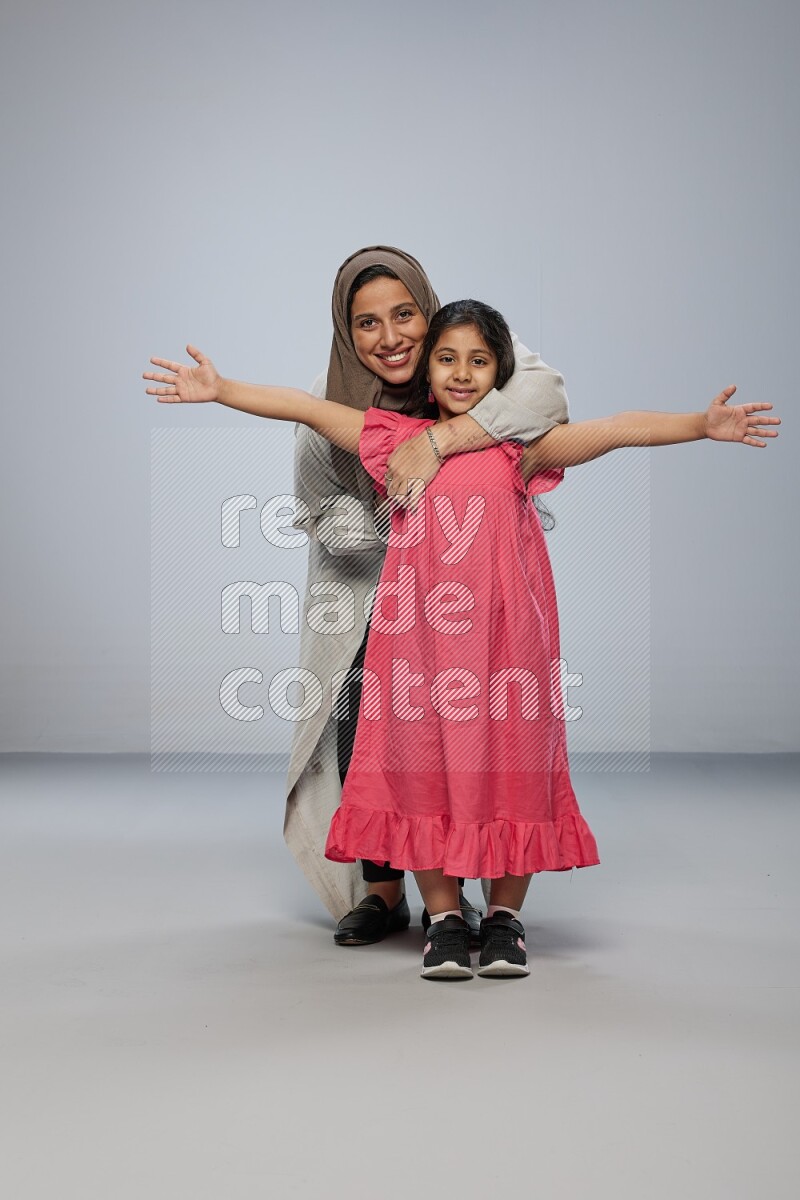 A girl and her mother interacting with the camera on gray background