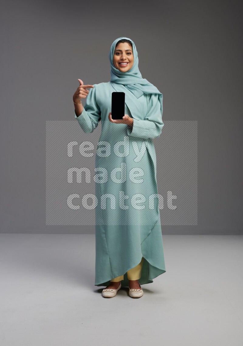 Saudi Woman wearing Abaya standing showing phone to camera on Gray background