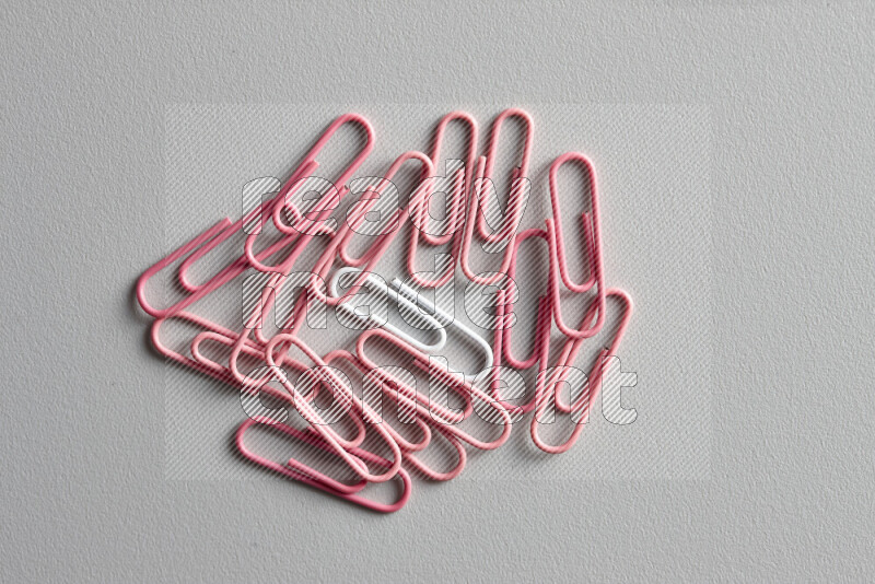 A bunch of pink paper clips with a different colored paper clip in the center on grey background