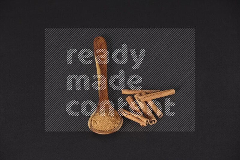 Cinnamon powder in a wooden ladle spoon beside it cinnamon sticks on the flooring on black background in different angles