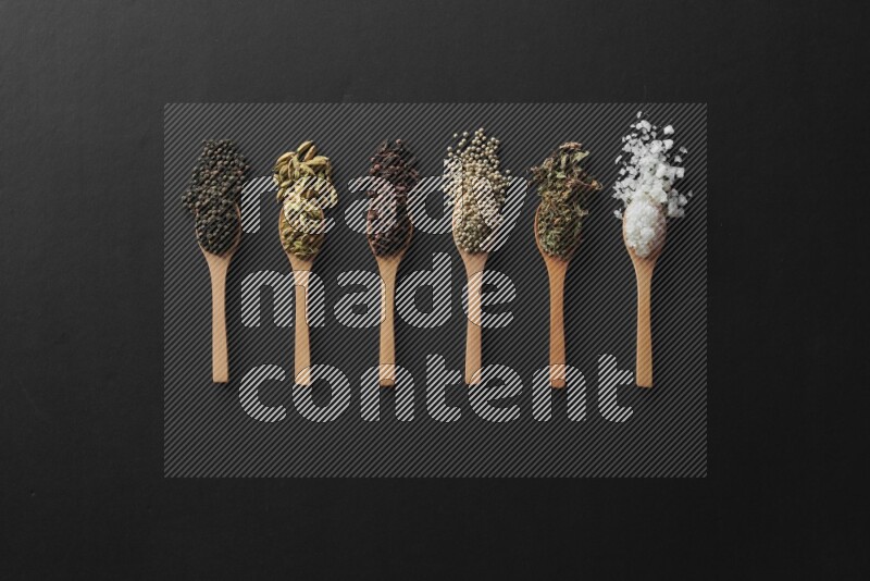 الفلفل الأبيض والقرنفل والهيل والملح والفلفل الأسود وريحان مجفف في معالق خشبية علي خلفية سوداء