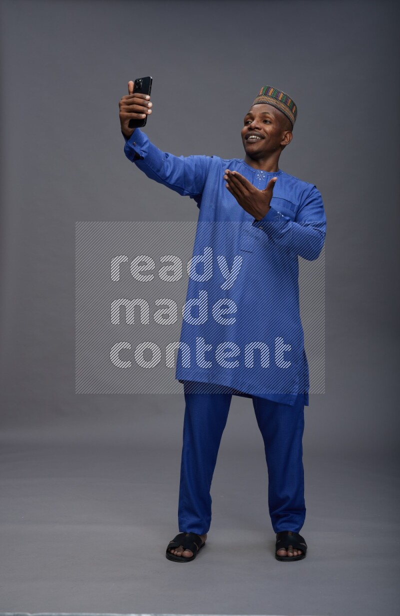 Man wearing Nigerian outfit standing taking selfie on gray background