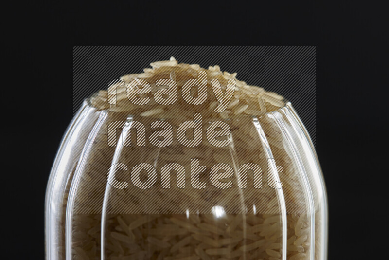 Basmati golden rice in a glass jar on black background