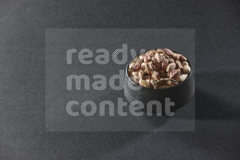 A black pottery bowl full of peeled pistachios on a black background in different angles