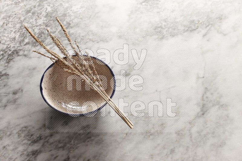 Wheat stalks on multicolored pottery bowl on grey marble background