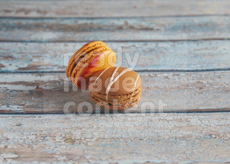 45º Shot of of two assorted Brown Irish Cream, and Orange Exotic macarons on light blue background
