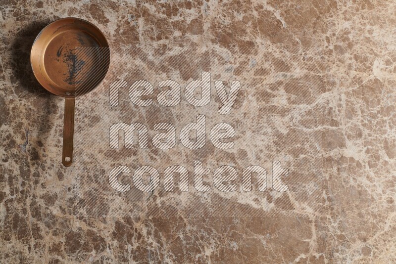 A small copper pan on beige marble background