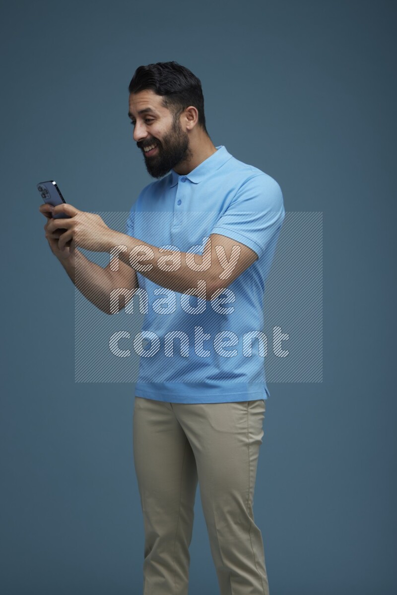 A man Texting on his phone in a blue background wearing a Blue shirt