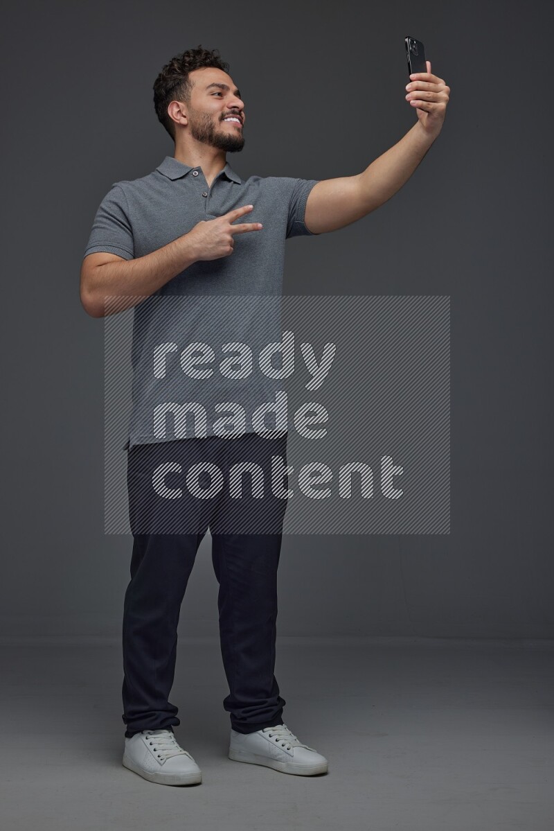 A man wearing casual and taking selfie with his phone different angles eye level on a gray background